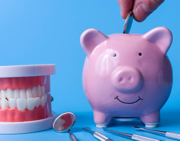 A piggy bank next to dental instruments on a blue background