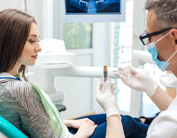 Dentist showing parts of a model implant to a patient with long brown hair