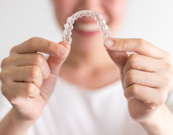 Smiling woman holding an Invisalign tray outdoors