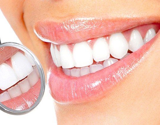 Closeup of a dental mirror reflecting a bright white smile